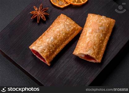 Delicious fresh crispy pie with cherry jam on a wooden cutting board on a dark concrete background