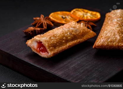 Delicious fresh crispy pie with cherry jam on a wooden cutting board on a dark concrete background