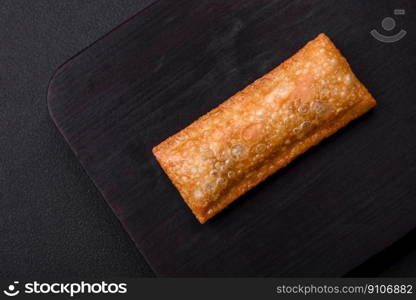 Delicious fresh crispy pie with cherry jam on a wooden cutting board on a dark concrete background