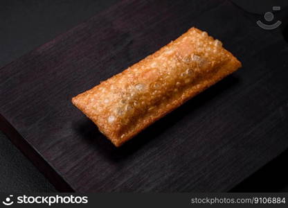 Delicious fresh crispy pie with cherry jam on a wooden cutting board on a dark concrete background