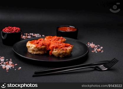 Delicious fresh cut≤ts or meatballs with sπces, herbs and tomato sauce on a dark concrete background