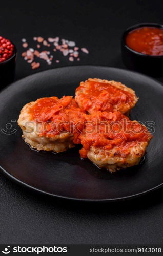 Delicious fresh cutlets or meatballs with spices, herbs and tomato sauce on a dark concrete background