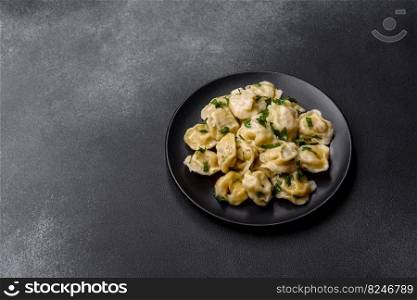 Delicious fresh dumplings with turkey meat, with spices and herbs, parsley on a black plate against a dark concrete background. Delicious fresh dumplings with turkey meat, with spices and herbs