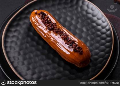Delicious fresh eclair with chocolate cream on a black ceramic plate on a dark concrete background