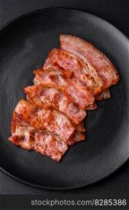 Delicious fresh fried bacon stripes with spices on a dark concrete background