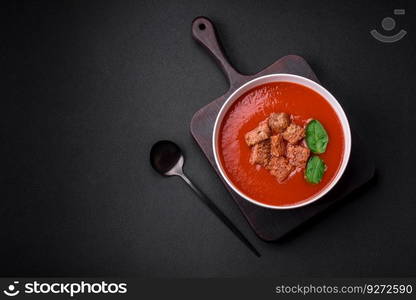 Delicious fresh gazpacho with breadcrumbs, sa<and sπces in a ceramic plate on a dark concrete background