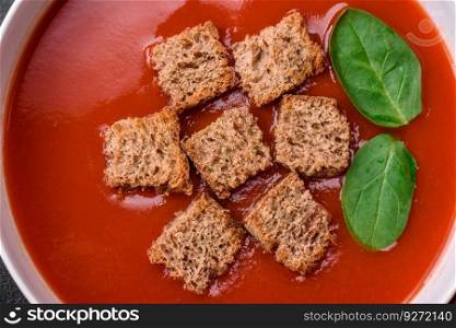 Delicious fresh gazpacho with breadcrumbs, salt and spices in a ceramic plate on a dark concrete background