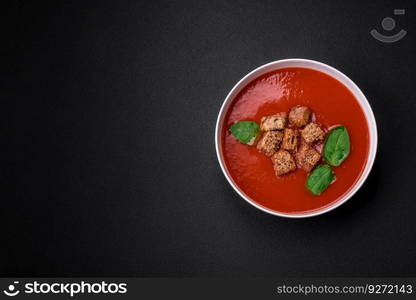 Delicious fresh gazpacho with breadcrumbs, salt and spices in a ceramic plate on a dark concrete background