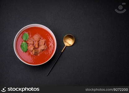 Delicious fresh gazpacho with breadcrumbs, salt and spices in a ceramic plate on a dark concrete background