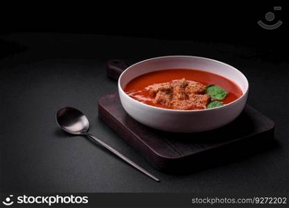 Delicious fresh gazpacho with breadcrumbs, salt and spices in a ceramic plate on a dark concrete background