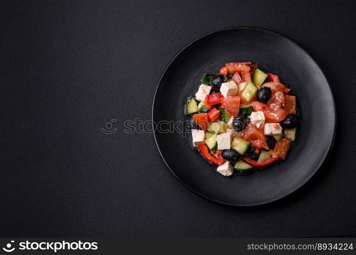 Delicious fresh Greek salad with olives, tomatoes, cucumbers, feta cheese, spices, herbs and olive oil on a black ceramic plate