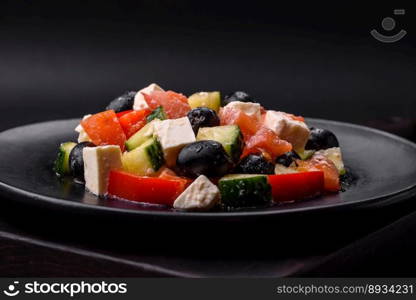 Delicious fresh Greek salad with olives, tomatoes, cucumbers, feta cheese, spices, herbs and olive oil on a black ceramic plate