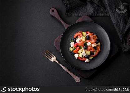 Delicious fresh Greek salad with olives, tomatoes, cucumbers, feta cheese, spices, herbs and olive oil on a black ceramic plate
