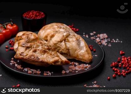 Delicious fresh grilled chicken fillet with salt, spices and herbs on a ceramic plate on a dark concrete background
