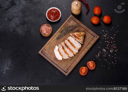 Delicious fresh grilled chicken fillet with spices and herbs on a dark concrete background. A dish cooked over fire. Delicious fresh grilled chicken fillet with spices and herbs on a dark concrete background