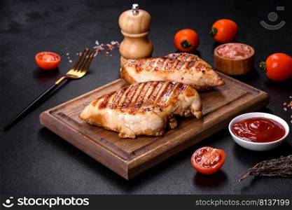 Delicious fresh grilled chicken fillet with spices and herbs on a dark concrete background. A dish cooked over fire. Delicious fresh grilled chicken fillet with spices and herbs on a dark concrete background