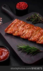 Delicious fresh grilled or smoked ribs with salt, spices and herbs on dark concrete background