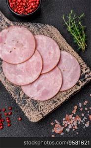 Delicious fresh ham cut into round slices with salt, spices and herbs on a dark concrete background