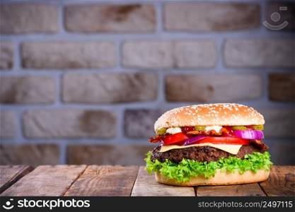 Delicious fresh hamburger on wooden table. Big burger in classic american style with hot grilled patty with melted cheese on top, tomato, onion and sauces.