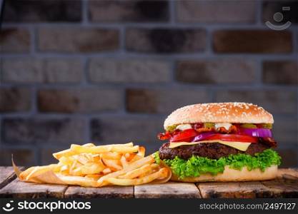 Delicious fresh hamburger with french fries on wooden table. Big burger in classic american style with hot grilled patty with melted cheese on top, tomato, onion, sauces and fried chips.