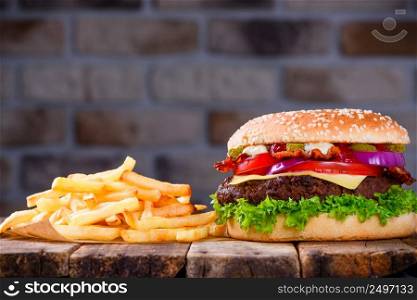 Delicious fresh hamburger with french fries on wooden table. Big burger in classic american style with hot grilled patty with melted cheese on top, tomato, onion, sauces and fried chips.