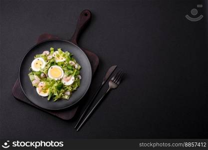 Delicious fresh healthy salad with shrimp, egg, lettuce and flax seeds on a black ceramic plate on a concrete background