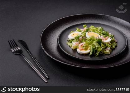 Delicious fresh healthy salad with shrimp, egg, lettuce and flax seeds on a black ceramic plate on a concrete background