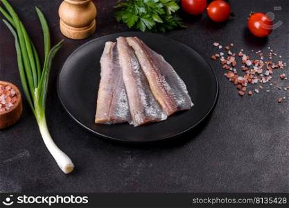 Delicious fresh herring fil≤t with sa<, sπces and herbs on a black plate against a dark concrete background. Delicious fresh herring fil≤t with sa<, sπces and herbs on a black plate