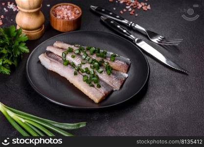Delicious fresh herring fillet with salt, spices and herbs on a black plate against a dark concrete background. Delicious fresh herring fillet with salt, spices and herbs on a black plate