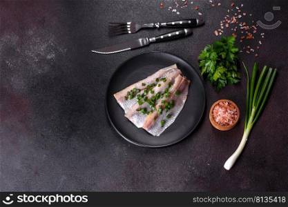 Delicious fresh herring fillet with salt, spices and herbs on a black plate against a dark concrete background. Delicious fresh herring fillet with salt, spices and herbs on a black plate