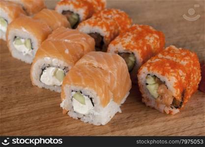 Delicious fresh Japanese sushi rolls . Set with salmon, eel , cheese, california, flying fish roe , red caviar , wasabi mustard Imber . On a wooden board.