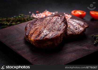 Delicious fresh juicy beef steak with spices and herbs on a dark concrete background. Grilled dish