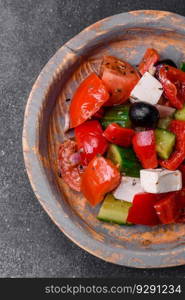 Delicious fresh juicy greek salad with feta cheese, olives, peppers, tomatoes, cucumber and onions on a gray concrete background