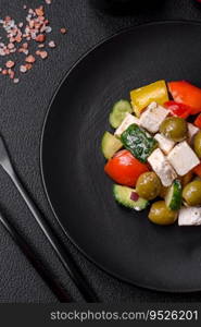 Delicious fresh, juicy Greek salad with feta cheese, olives, tomatoes, cucumber, pepper, salt and spices on a dark concrete background