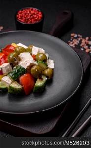 Delicious fresh, juicy Greek salad with feta cheese, olives, tomatoes, cucumber, pepper, salt and spices on a dark concrete background
