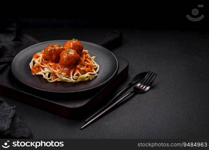 Delicious fresh meatballs and pasta in tomato sauce with salt, spices and herbs on a dark concrete background