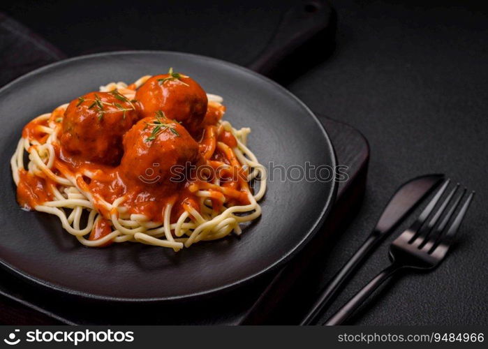 Delicious fresh meatballs and pasta in tomato sauce with salt, spices and herbs on a dark concrete background