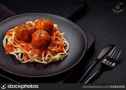 Delicious fresh meatballs and pasta in tomato sauce with salt, spices and herbs on a dark concrete background