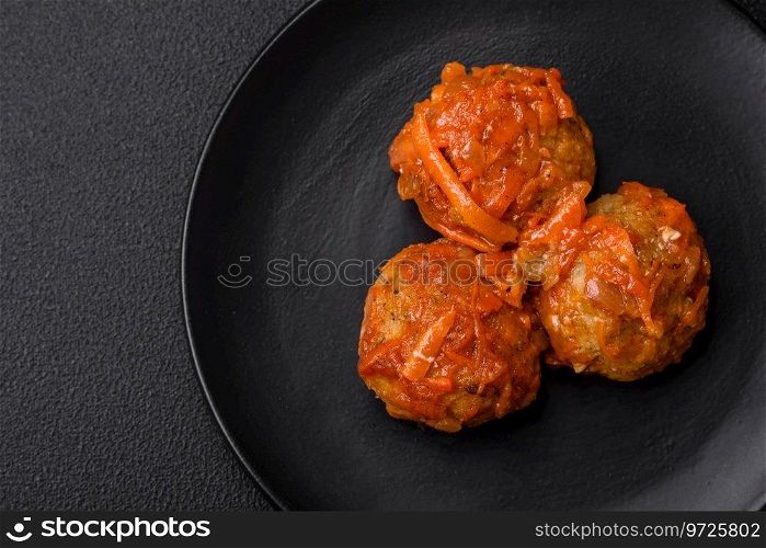 Delicious fresh meatballs from minced meat or fish with tomato sauce, carrots, onions, salt and spices on a dark concrete background