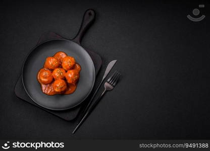 Delicious fresh meatballs in tomato sauce with salt, spices and herbs on a dark concrete background