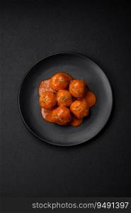 Delicious fresh meatballs in tomato sauce with salt, spices and herbs on a dark concrete background