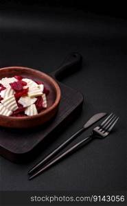 Delicious fresh mozzarella and boiled beets cut into slices on a round ceramic plate on a dark concrete background