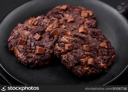 Delicious fresh oatmeal round cookies with chocolate on a black ceramic plate on a dark concrete background