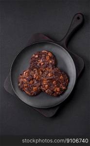 Delicious fresh oatmeal round cookies with chocolate on a black ceramic plate on a dark concrete background