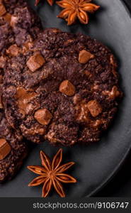 Delicious fresh oatmeal round cookies with chocolate on a black ceramic plate on a dark concrete background