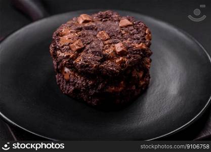 Delicious fresh oatmeal round cookies with chocolate on a black ceramic plate on a dark concrete background