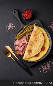 Delicious fresh omelet with cherry tomatoes, bacon, asparagus and spices on a dark concrete background
