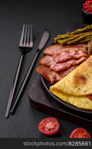 Delicious fresh omelet with cherry tomatoes, bacon, asparagus and spices on a dark concrete background