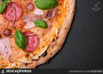 Delicious fresh oven baked pizza with salami, meat, cheese, tomatoes, spices and herbs on a dark concrete background. Delicious fresh oven baked pizza with salami, meat, cheese, tomatoes