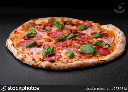 Delicious fresh oven baked pizza with salami, meat, cheese, tomatoes, spices and herbs on a dark concrete background. Delicious fresh oven baked pizza with salami, meat, cheese, tomatoes